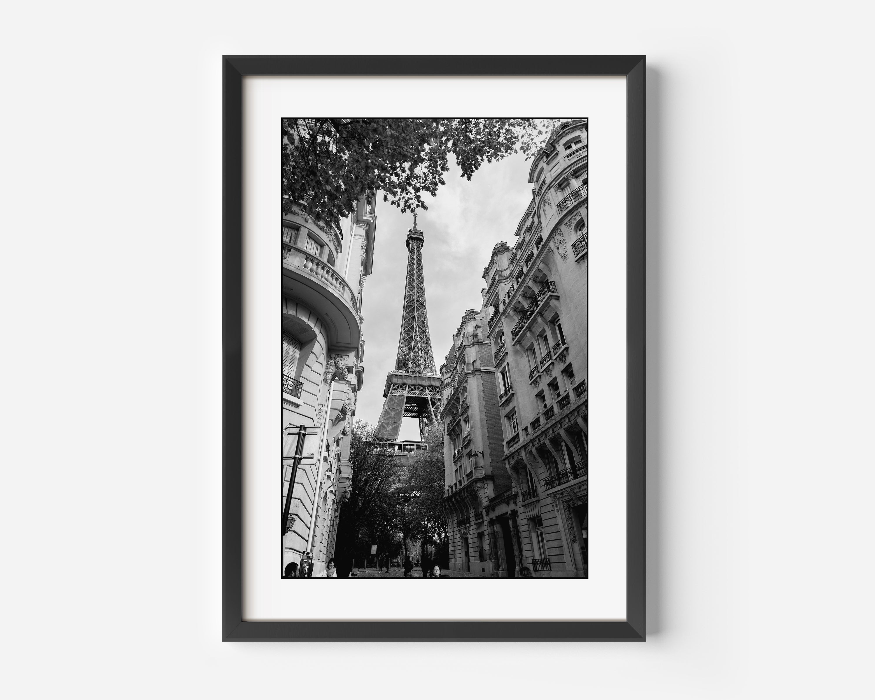 Black and white photograph of the Eiffel Tower through a city street in Paris, France